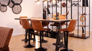 A modern dining area with a wooden table, six upholstered chairs, and a black metal partition with shelves. - "Industrial Sanctum" by Interhome (Brussels)