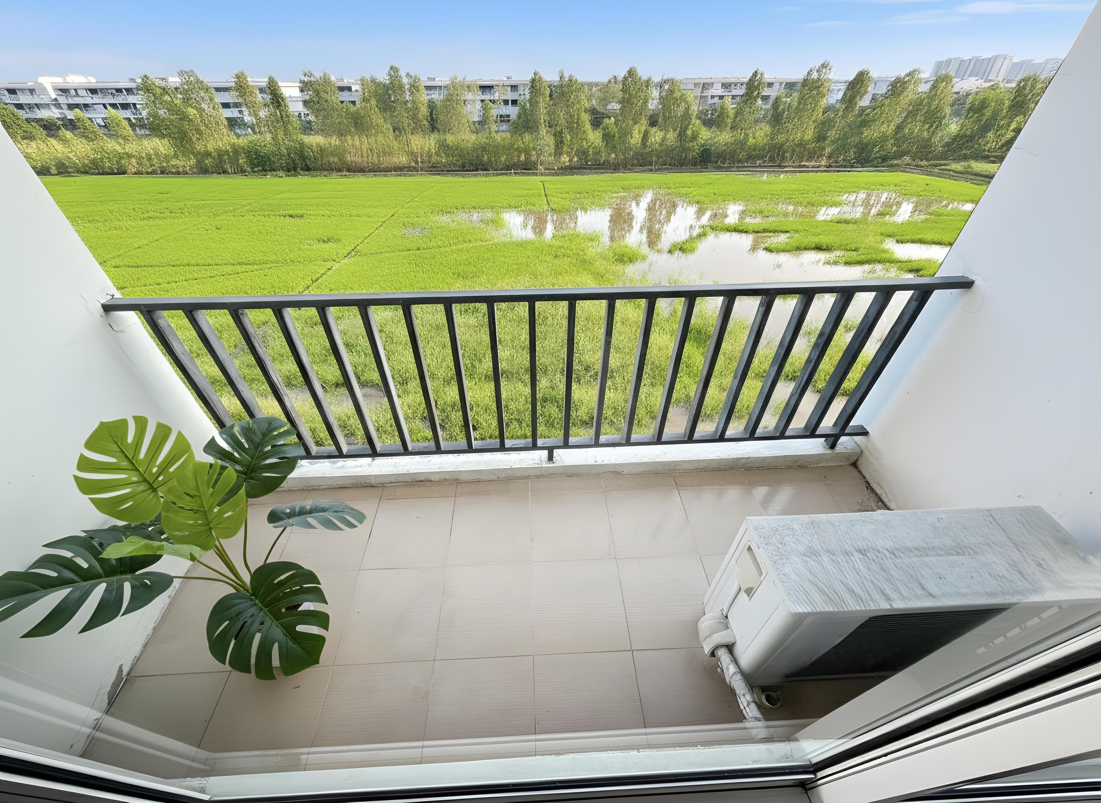 A balcony with a view of a green field and buildings in the distance.