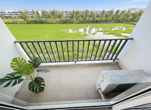 Un balcon donnant sur un champ verdoyant et sur des bâtiments situés au loin.
