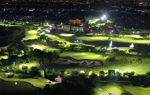 Un campo de golf de noche con zonas de juego iluminadas, bunkers y un club house.
