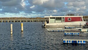 Eine Anlegestelle mit einem rot-weißen Gebäude, Holzpfählen und schwimmenden Stegen im Wasser.