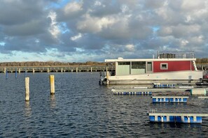 Eine Anlegestelle mit einem rot-weißen Gebäude, Holzpfählen und schwimmenden Stegen im Wasser.