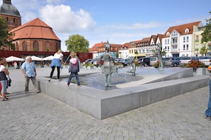 Ein öffentlicher Platz mit einem Brunnen, Personen und historischen Gebäuden im Hintergrund.