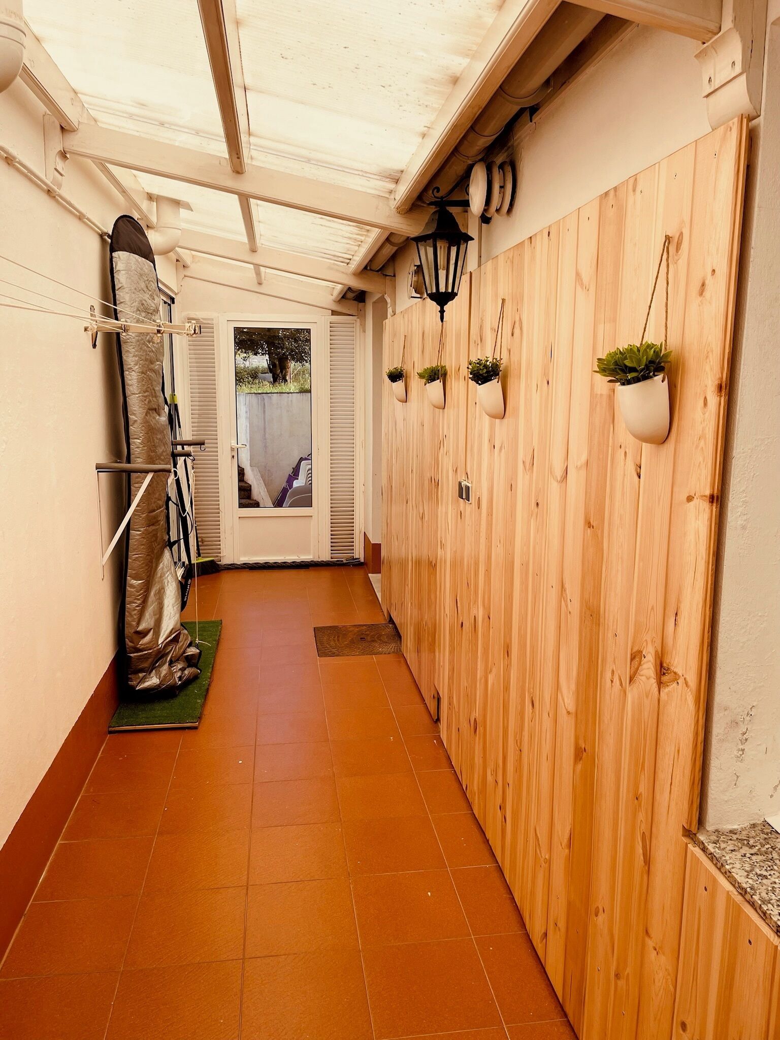 Un corridoio stretto con pareti rivestite in legno, pavimento piastrellato e una porta che dà su uno spazio esterno.