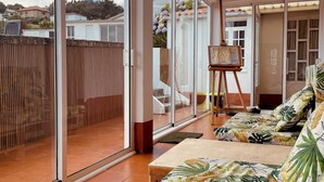 A spacious living room with large windows, a wooden floor, and a sofa with tropical leaf patterns.