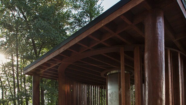 A covered pavilion with a concrete floor, surrounded by trees.