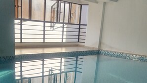 En inomhuspool med klart, blått vatten, kaklat golv och ett metallräcke.