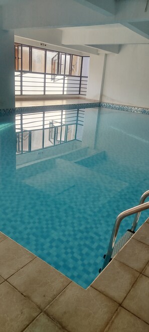 Ein Innenpool mit klarem, blauem Wasser, gefliestem Boden und einer Metallhandstange.