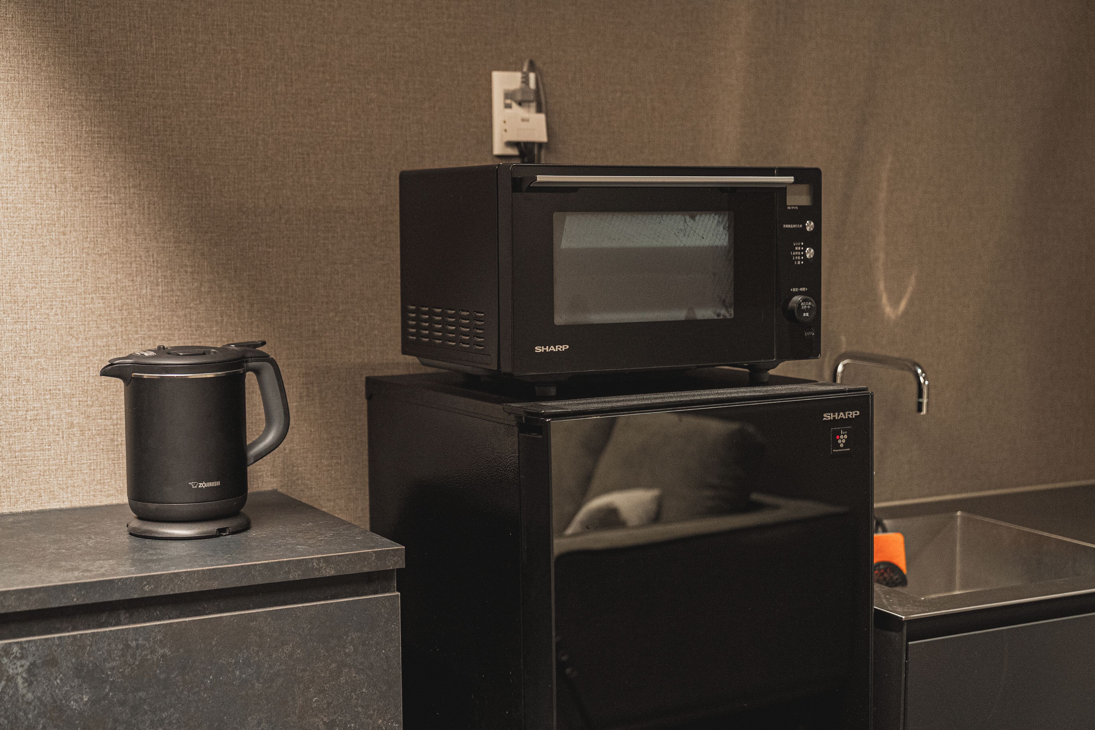 Une cuisine avec un four à micro-ondes posé sur le dessus d’un réfrigérateur, une machine à café et un évier.