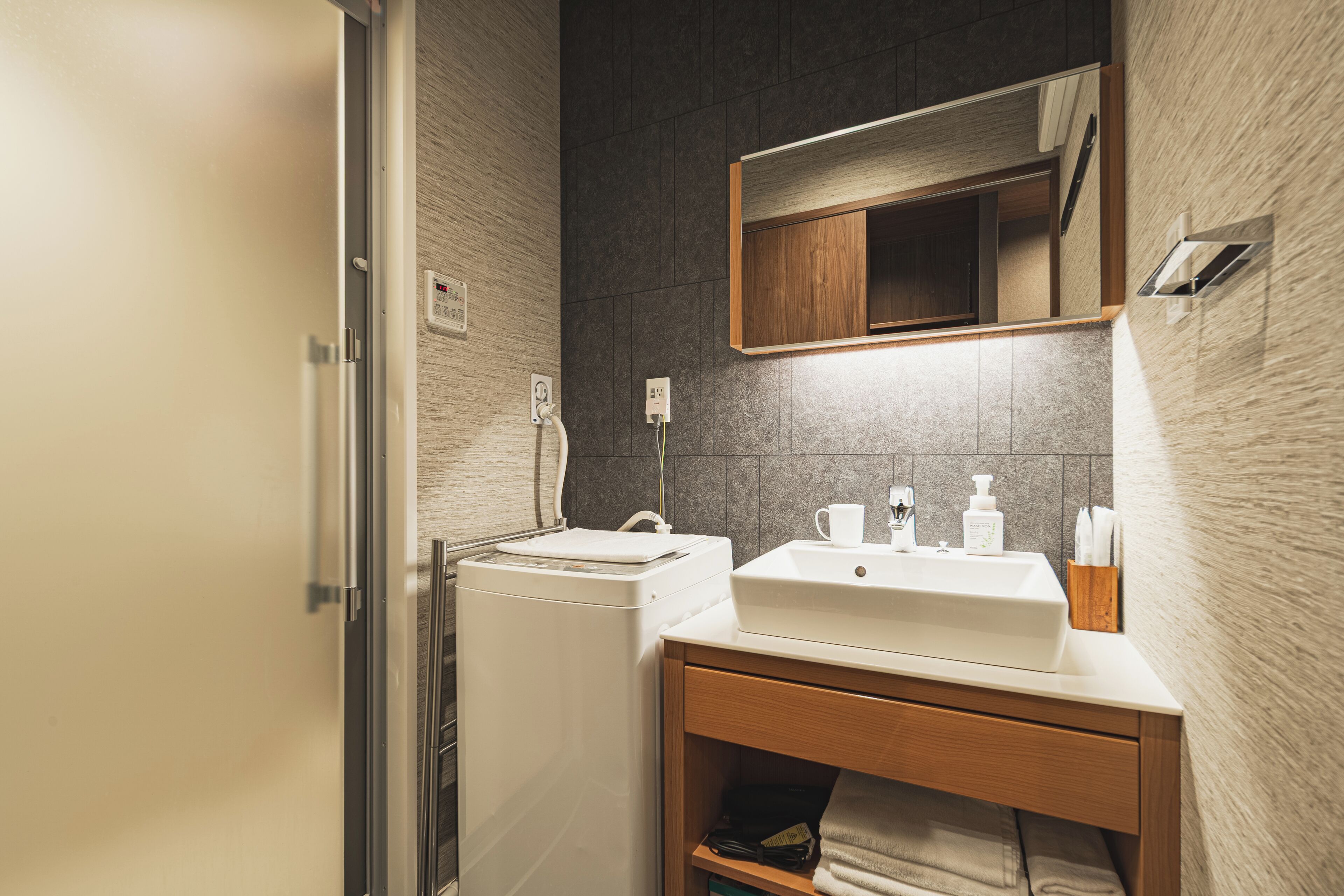 Une salle de bain moderne équipée d’un lave-linge intégré, d’un lavabo avec un miroir au-dessus et d’un porte-serviettes.