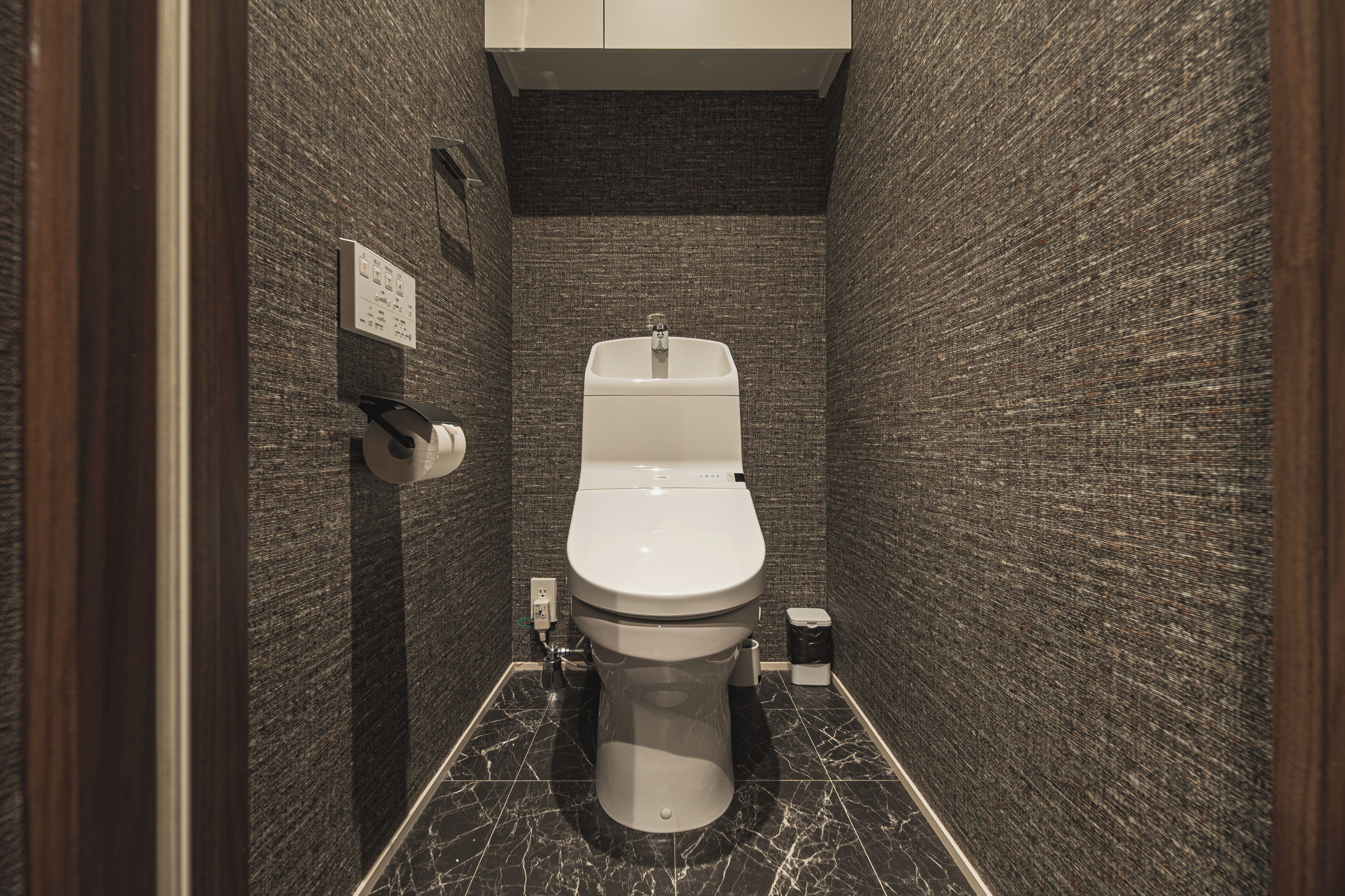 A compact bathroom with a modern toilet, a hand dryer, and a trash bin.