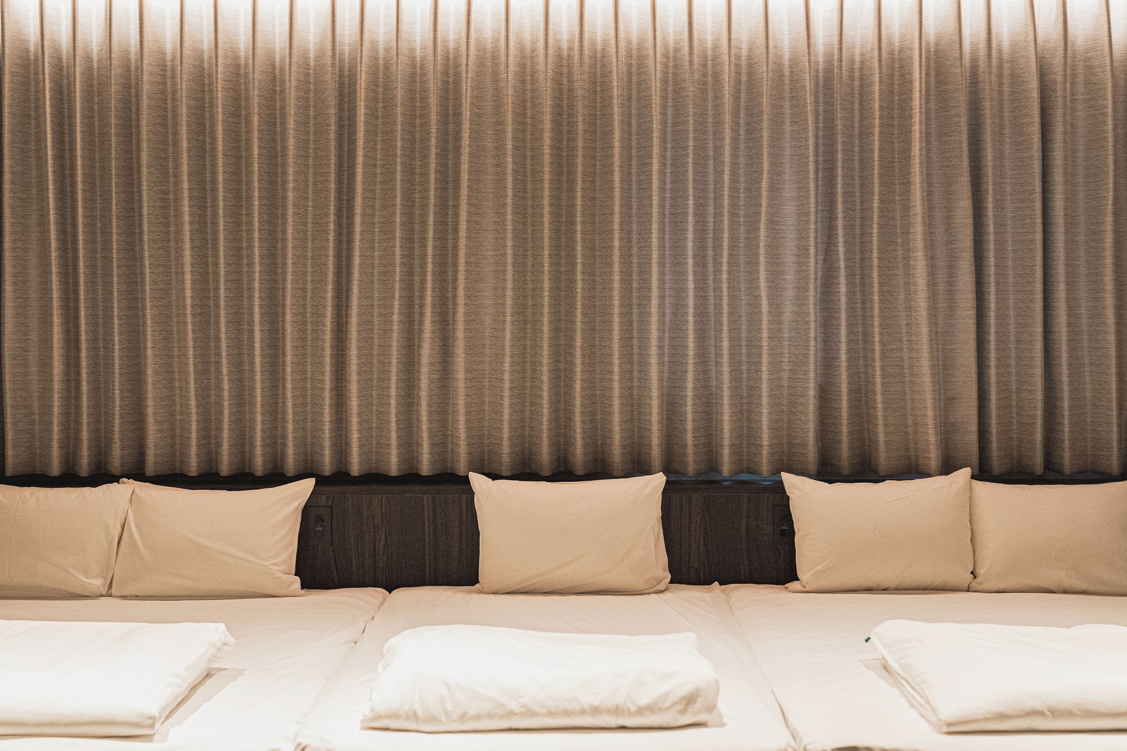Una habitación de hotel con una cama grande, ropa de cama color beige y un telón de fondo de cortina.