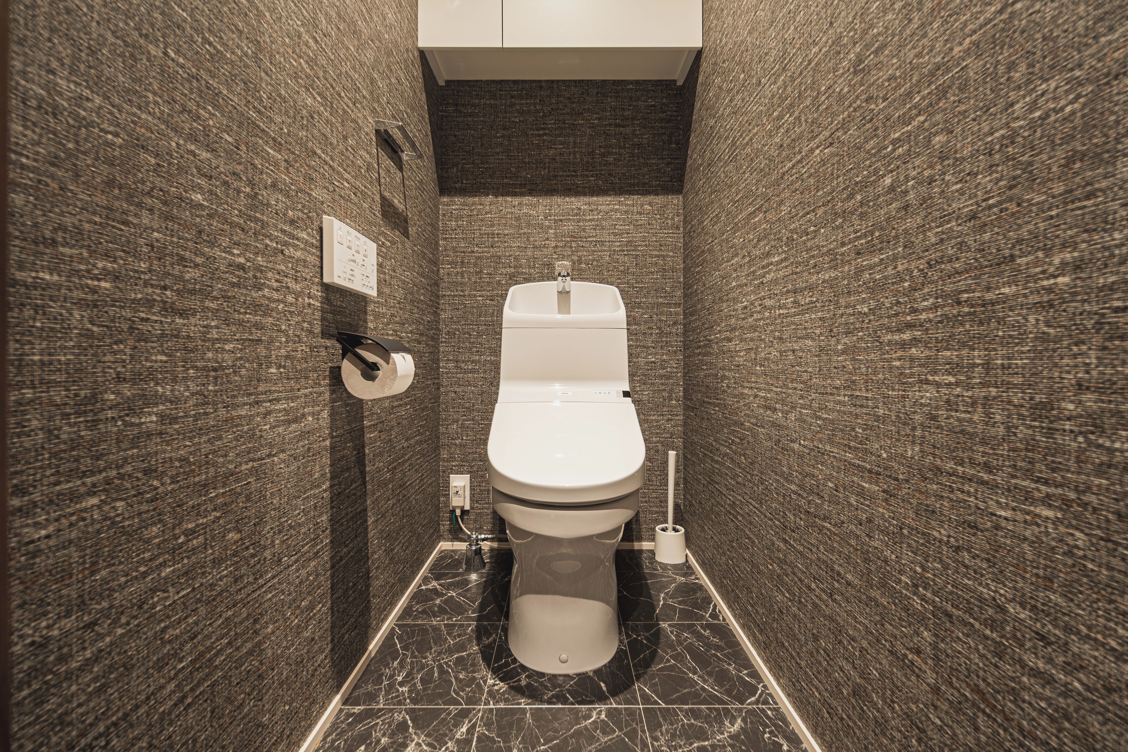 A compact bathroom with a toilet, a hand dryer, and a paper towel dispenser on the wall.