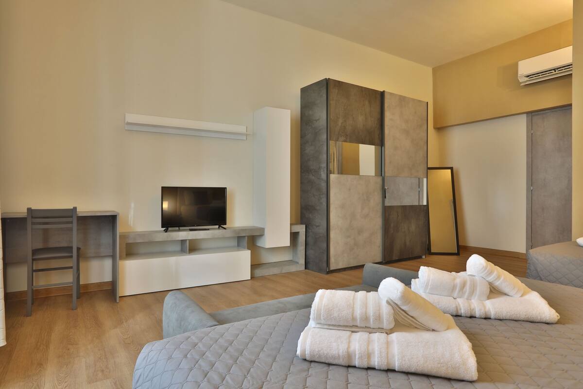 A modern hotel room with a flat-screen TV, a large mirror, and neatly folded towels on the bed.