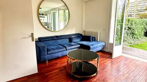 A modern living room with a blue sectional sofa, a round coffee table, and a large mirror on the wall. - Exceptional apartment with private garden (Neuilly-sur-Seine)