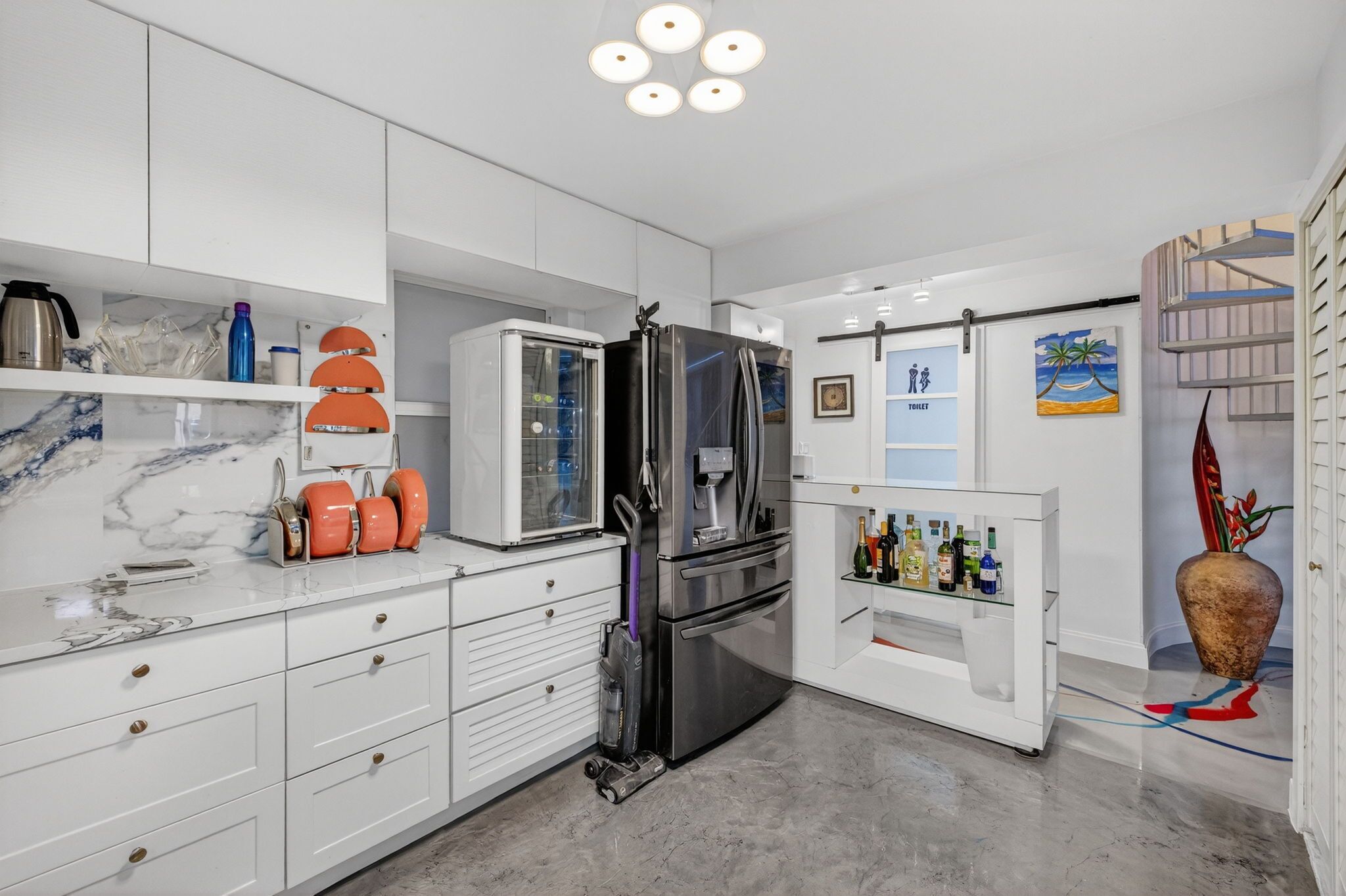 A modern kitchen with white cabinetry, a stainless steel refrigerator, and a marble countertop.