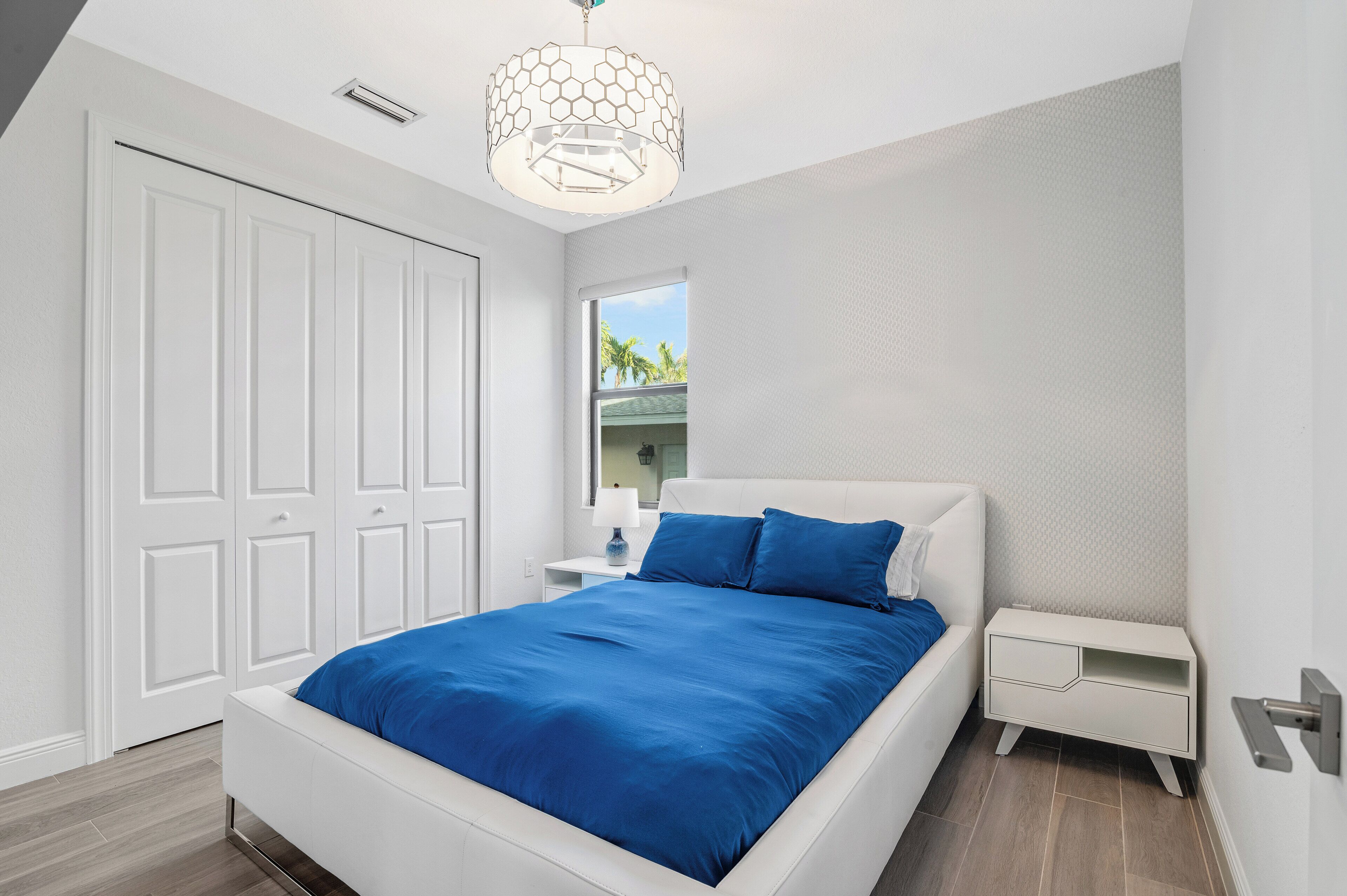 A bedroom with a white bed, blue bedding, a white nightstand, a white dresser, and a ceiling light fixture.