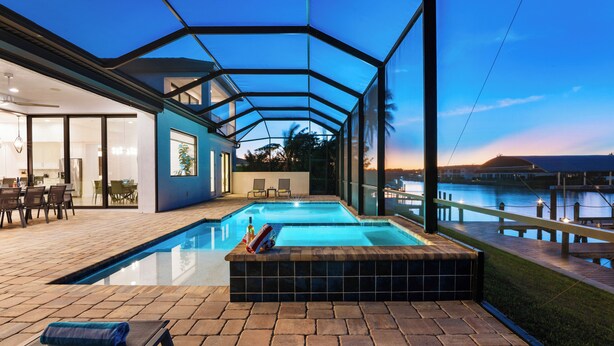 Uma piscina com cobertura de vidro, área de estar com cadeiras e vista para a água.