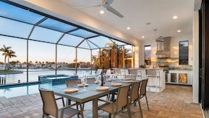 Cozinha moderna com uma ilha grande, área de jantar com vista para a piscina e um terraço com piscina.