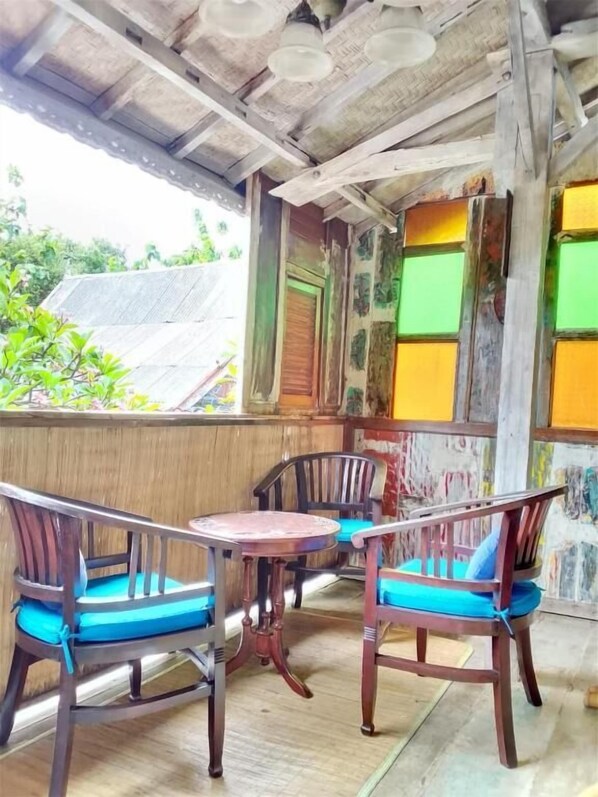 Un espace extérieur abrité, aménagé avec des chaises et une table en bois, une porte en bois et offrant une vue sur la verdure.