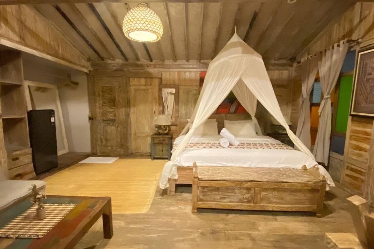 Une pièce rustique avec un lit en bois, un banc, une petite table et un luminaire suspendu.