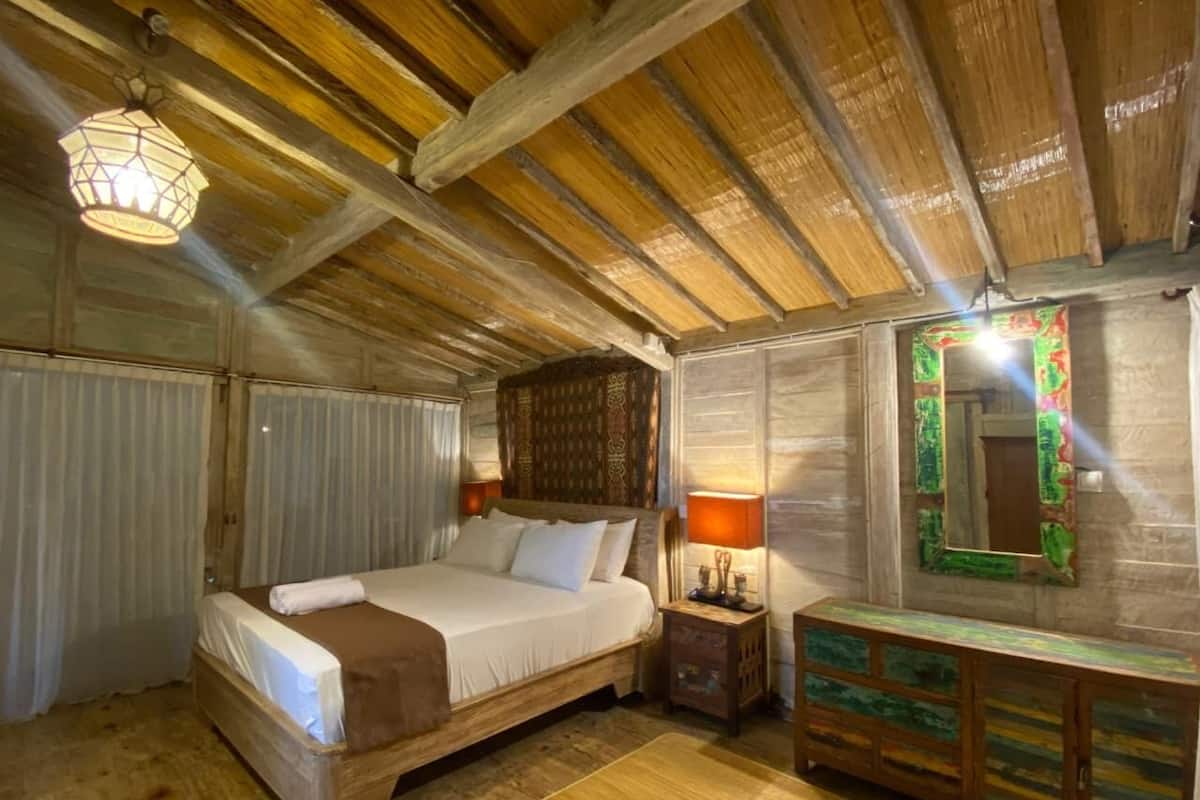 Une pièce aux murs en bois, avec un lit, une lampe de chevet et un miroir doté d’un cadre coloré.