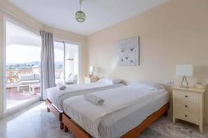 Ett hotellrum med två sängar, en balkong med utemöbler och ett stort fönster.