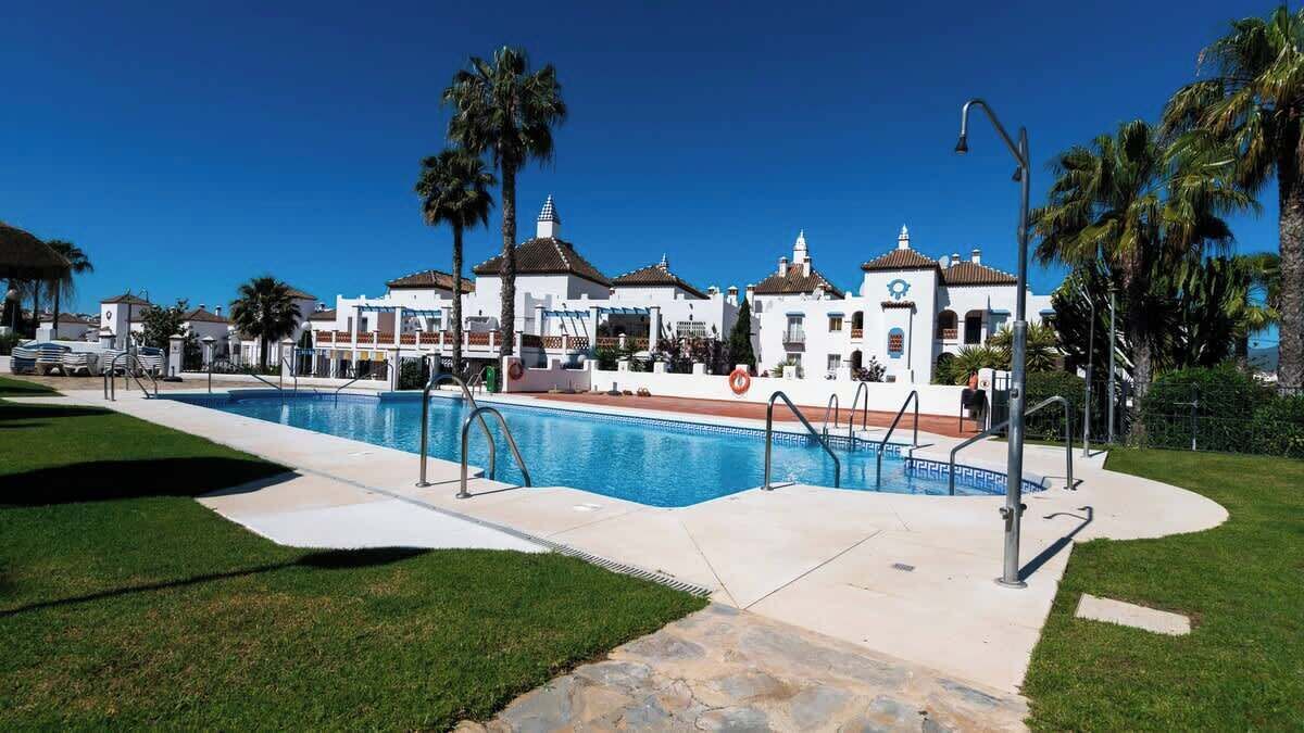 Una piscina con agua cristalina azul, rodeada de un césped cuidado y palmeras.