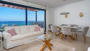 Un salon moderne avec une table basse en verre, un canapé blanc et un coin repas comprenant des chaises et une table en verre.