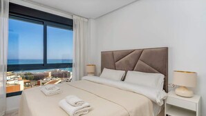 Une chambre d’hôtel avec un grand lit, une table de chevet et une vue sur la ville et la mer.