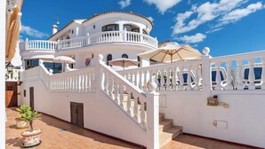 Un immeuble blanc à plusieurs étages, doté d’un balcon incurvé, d’un escalier et de parasols d’extérieur.