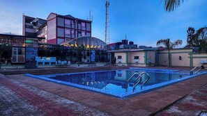 A swimming pool with a glass enclosure, surrounded by buildings and a palm tree.