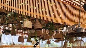Un café chaleureux avec des plafonds aux lambris en bois, des lampes suspendues en osier et des sièges rembourrés de tissu rouge et gris.