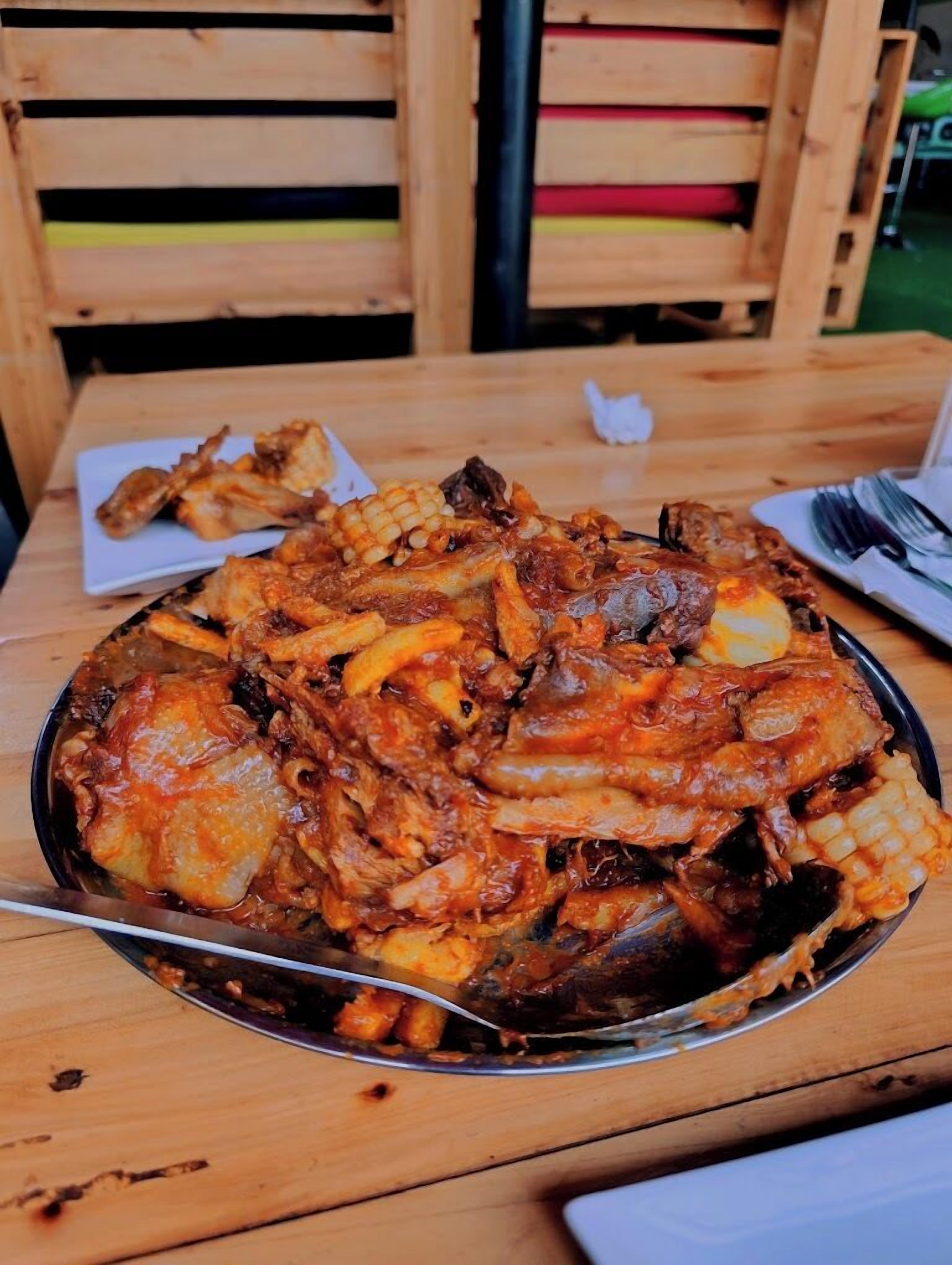 A large metal serving dish filled with a variety of meats and vegetables, placed on a wooden table.