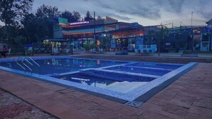 Une piscine dotée d’une terrasse carrelée, entourée d’un bâtiment sur lequel est apposée une enseigne indiquant qu’il s’agit d’un hôtel.