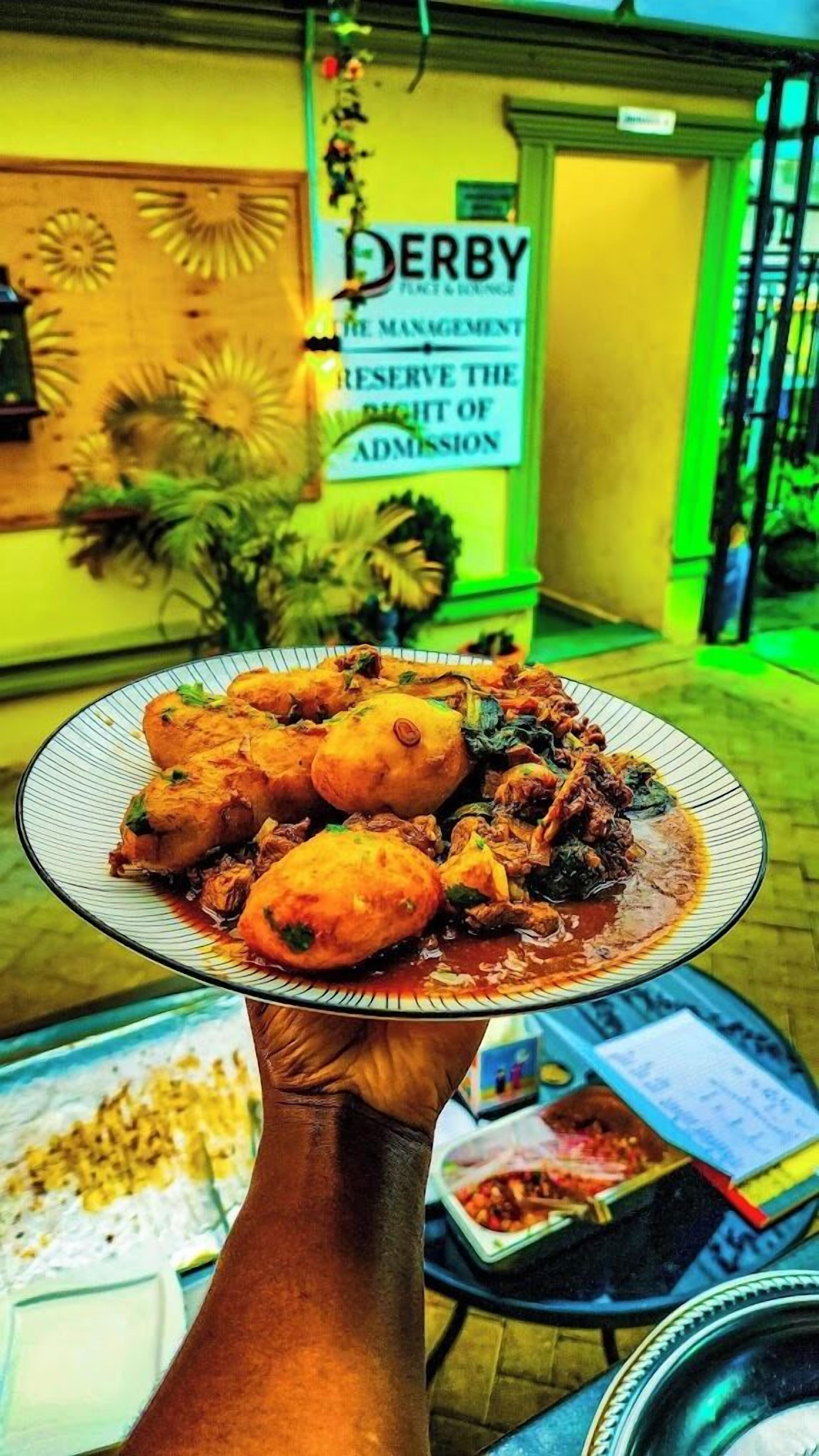 A plate of food being held in front of a sign that reads "DERBY THE MANAGEMENT RESERVE THE RIGHT OF ADMISSION."