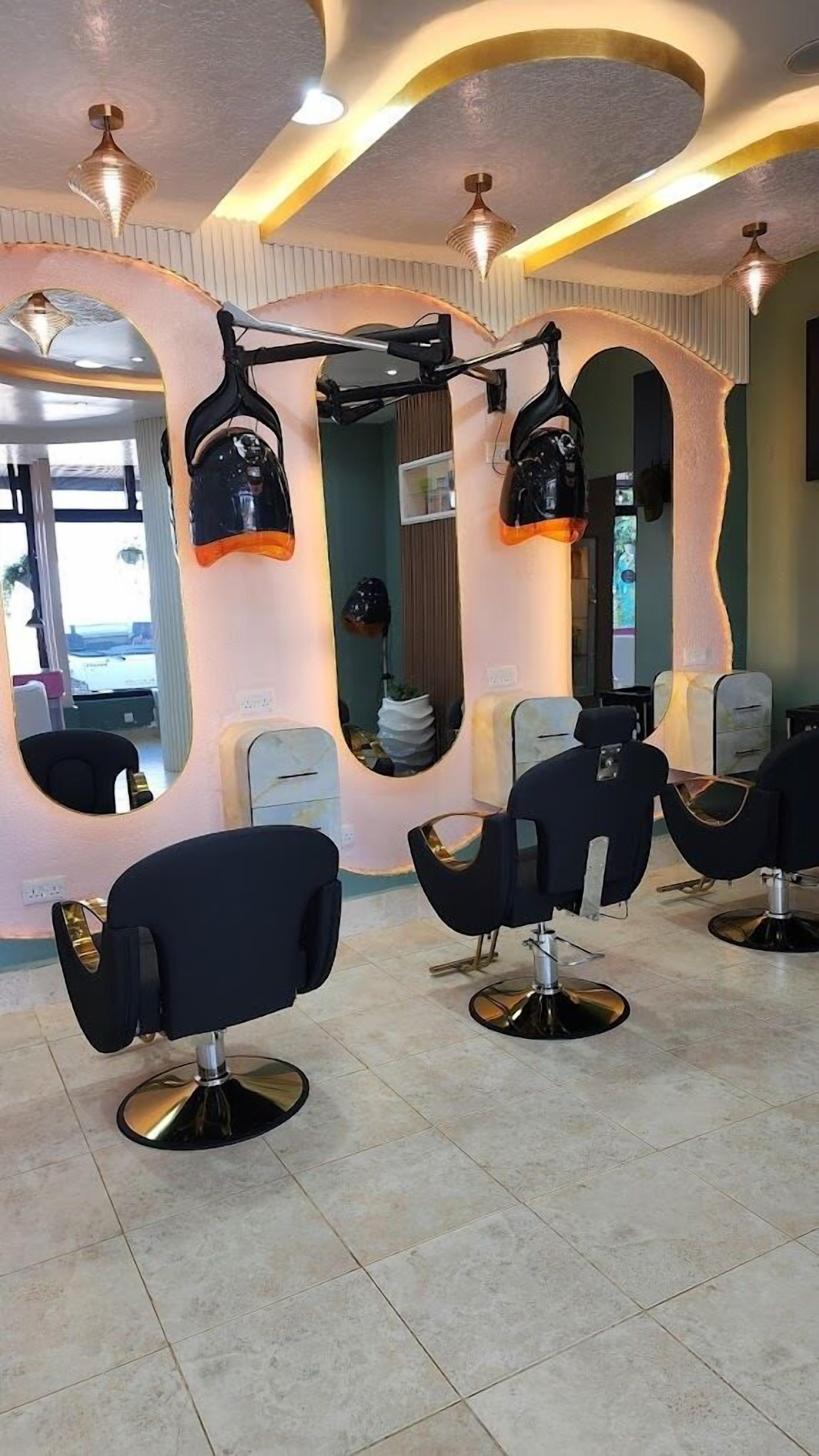 Un salón de belleza con varias sillas de peluquería negras, un espejo grande e iluminación empotrada en el techo.