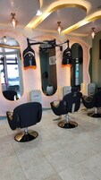 Un salón de belleza con varias sillas de peluquería negras, un espejo grande e iluminación empotrada en el techo.