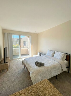 A hotel room with a large bed, a TV on a wooden stand, and a sliding glass door leading to a balcony. - 1 Bedroom Sunset Escape In Marina Del Rey (Marina del Rey)