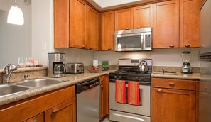 A modern kitchen with wooden cabinets, stainless steel appliances, a dishwasher, and a red towel hanging on the oven. - 1 Bedroom Sunset Escape In Marina Del Rey (Marina del Rey)