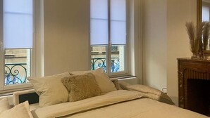Een slaapkamer met een bed, een raam met zonwering, een kroonluchter en een open haard.