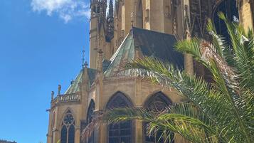 A historic cathedral with Gothic architecture, featuring pointed arches and a large rose window. Palm trees are in the foreground, and there are people walking around.