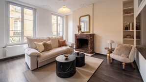 Een woonkamer met een bank, twee bijzettafels, een open haard en een boekenkast.