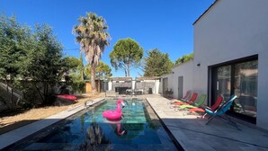 Ein moderner Außenpool mit einem rosa Flamingo-Schwimmpfaugel, umgeben von einer Terrasse mit bunten Liegestühlen und einer Steinmauer.