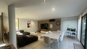 Ein modernes Wohnzimmer mit einer Couch, einem Esstisch, Stühlen, einem Fernseher und einem großen Fenster.