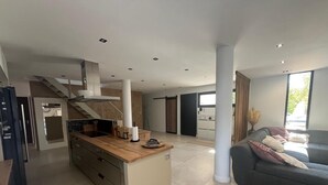 Eine moderne Küche mit Kochinsel, ein Essbereich inklusive Sofa und eine Treppe zu einer weiteren Ebene.