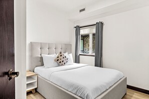 Ein Schlafzimmer mit Bett, Kopfstütze, einem Fenster mit Vorhängen und einer Tür.