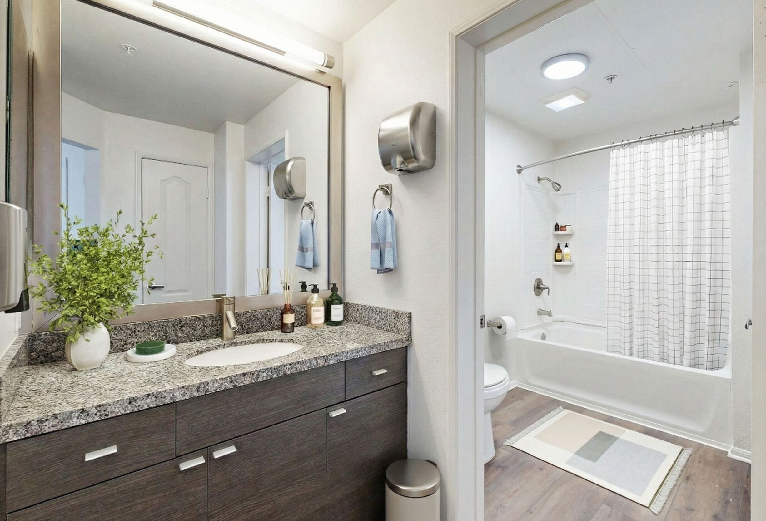 Een badkamer met een granieten aanrecht, een wastafel, een spiegel, een handdoekhouder, een douchegordijn en een toilet.