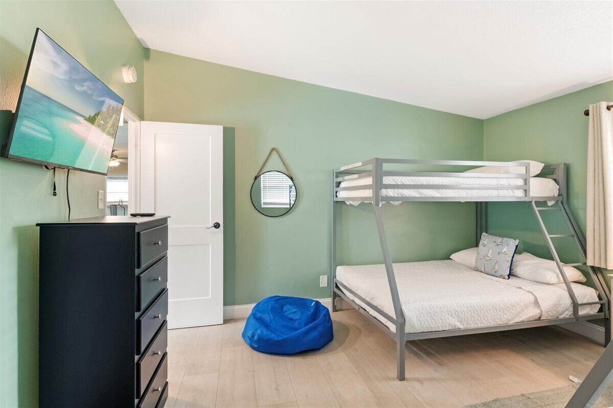 Une chambre avec un lit superposé, un téléviseur fixé au mur, une commode et un fauteuil en forme de poire bleu.