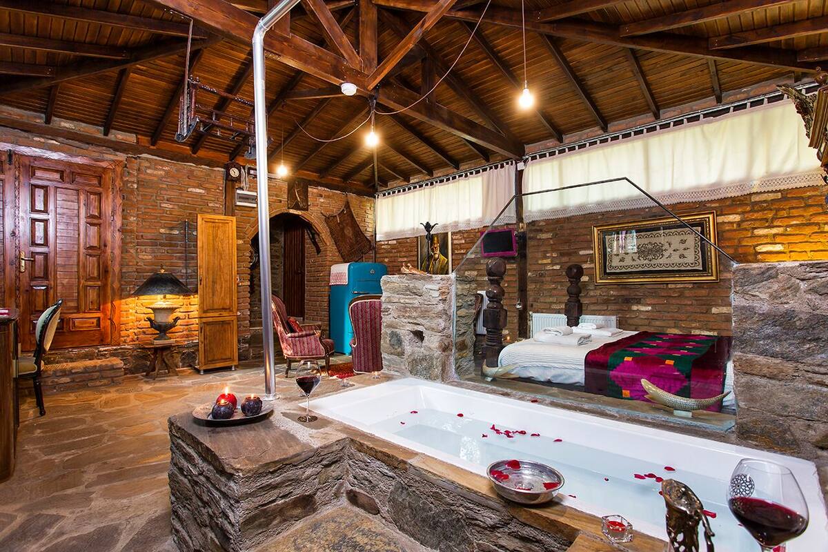 A rustic room with a stone fireplace, a large bathtub with rose petals, and a wooden ceiling.